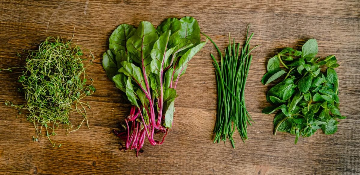 A vibrant selection of fresh herbs and greens neatly arranged on a wooden tabletop.