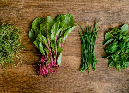A vibrant selection of fresh herbs and greens neatly arranged on a wooden tabletop.