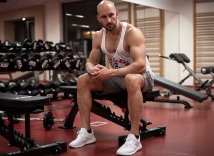 Strong, determined man in white tank top sitting in gym, showcasing fitness and strength.